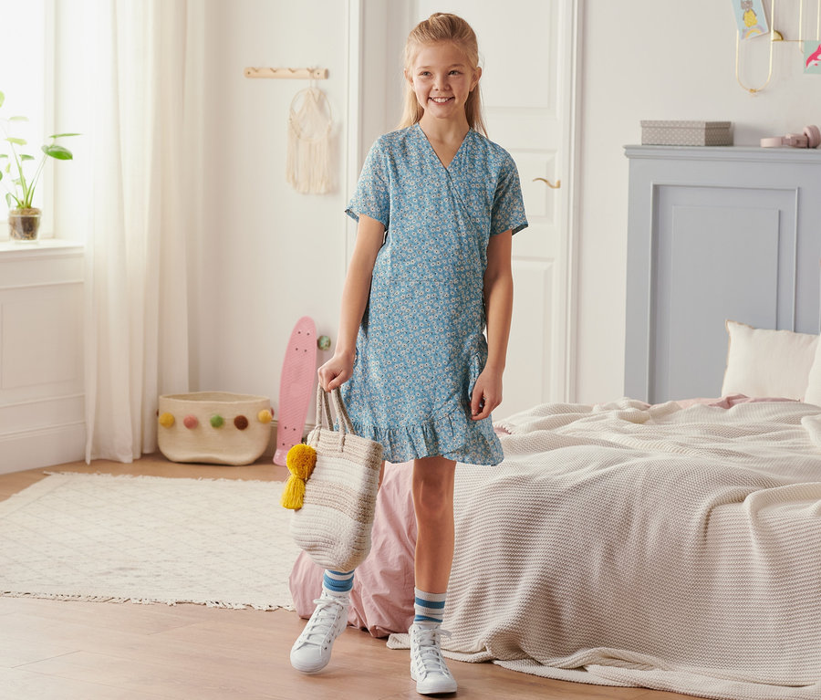 Lächelndes Mädchen steht im Zimmer und trägt ein Wickelkleid.