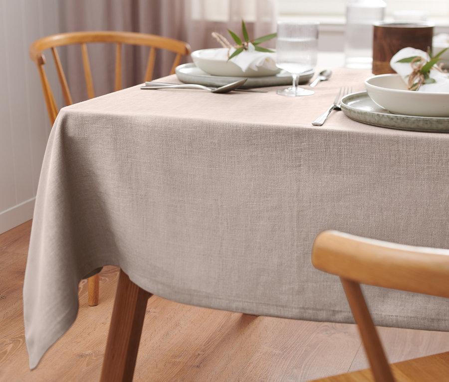 Detailansicht eines gedeckten Tisches mit einer Premium-Leinen-Tischdecke in Beige. Auf der Tischdecke befinden sich Teller, Gläser und Besteck.