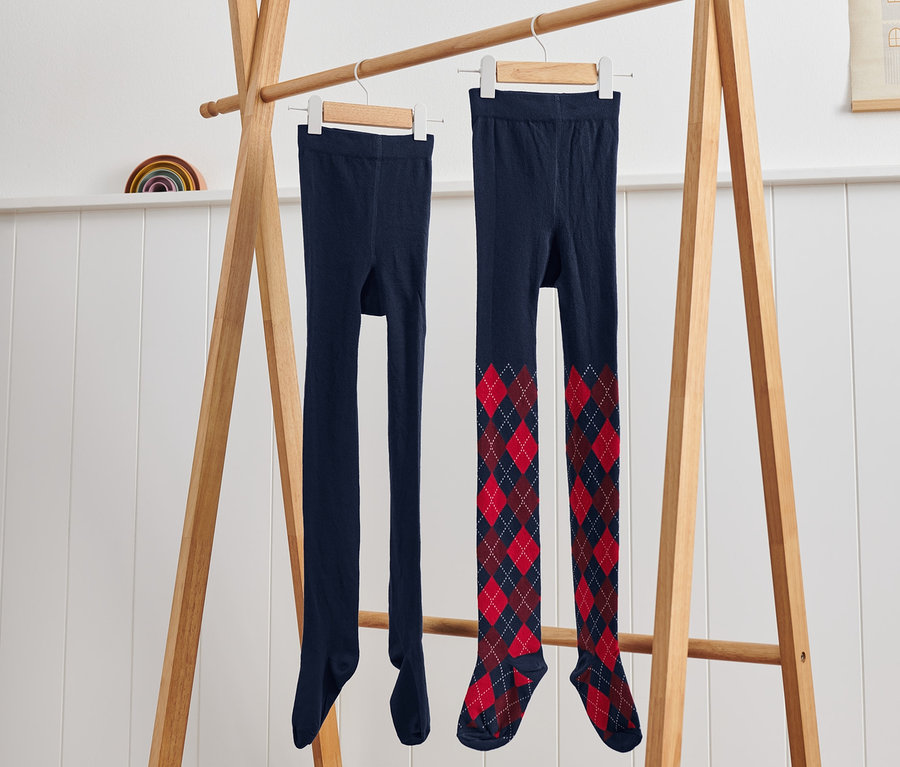 Zwei Kinder-Strumpfhosen mit Argyle-Muster hängen auf einem Holzständer.