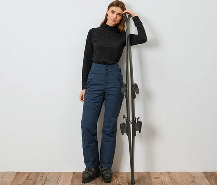 Frau lehnt an Ski und trägt eine blaue High-Waist-Skihose.