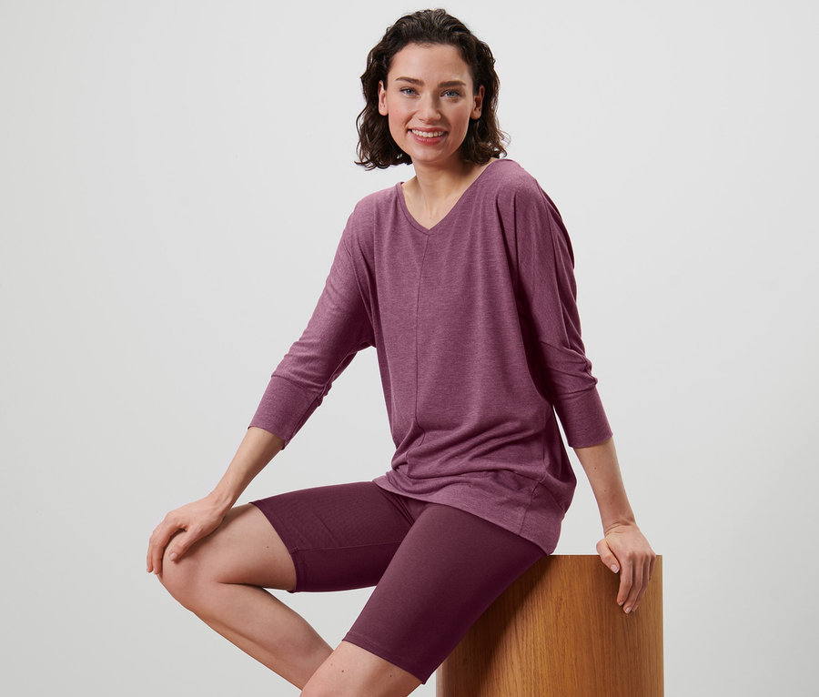 Frau sitzt auf einem Hocker und trägt ein Yogashirt in Mauve und Sportradler.
