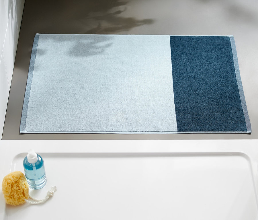 Ein blauer Jacquard-Duschvorleger liegt auf dem Boden neben einer Duschkabine.