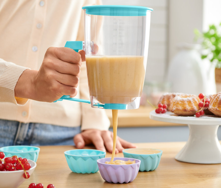 Frau portioniert Teig mit einem Teigportionierer in Silikon-Muffinförmchen.