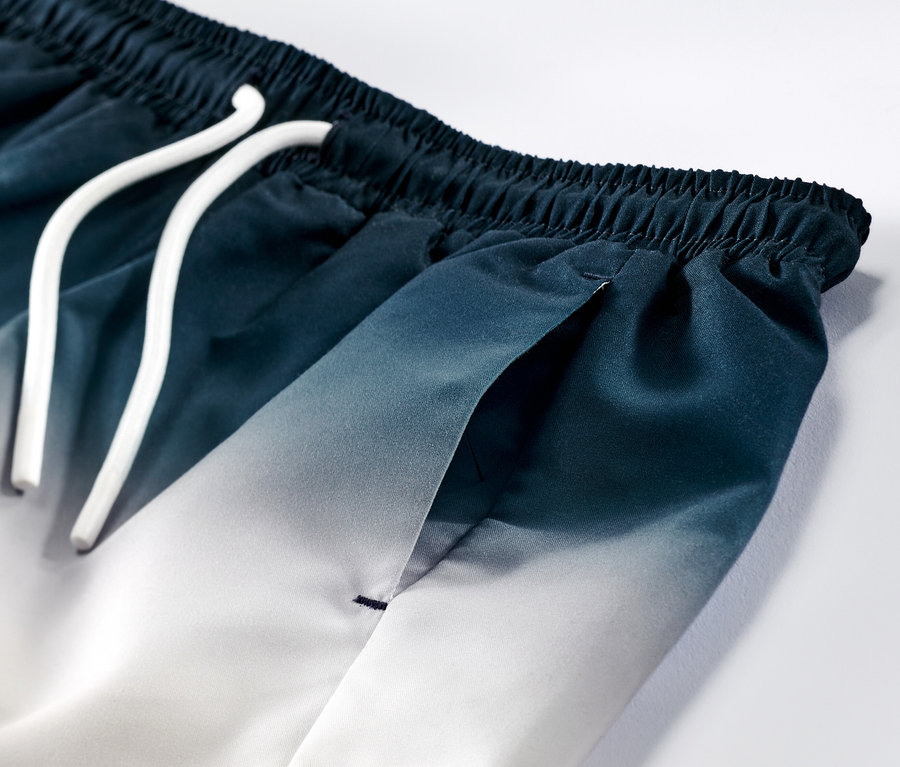 Detailaufnahme von Kinder-Boardshorts mit blau-weißem Farbverlauf und weißer Kordel.