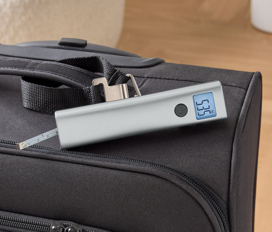 Eine digitale Kofferwaage liegt auf einem schwarzen Koffer.