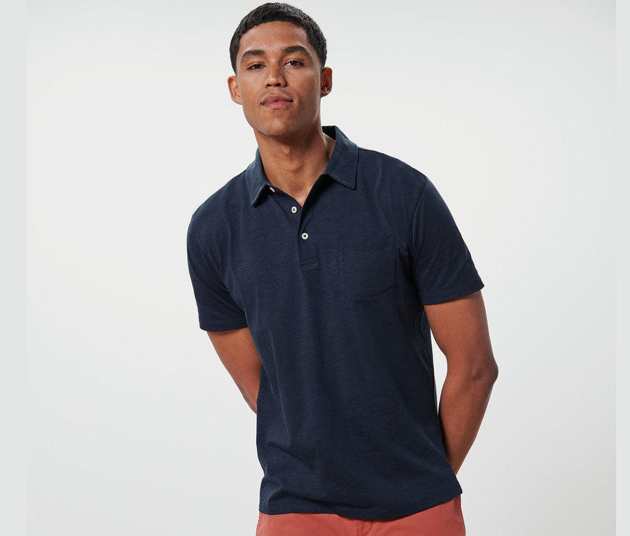 Mann posiert in marineblauem Jersey-Poloshirt und orangefarbenen Shorts.