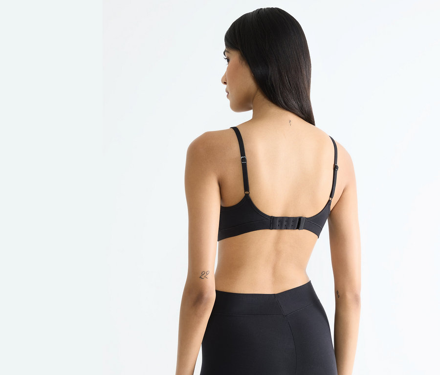 Rückansicht einer Frau mit langen Haaren, die einen schwarzen BH und schwarze Leggings trägt.