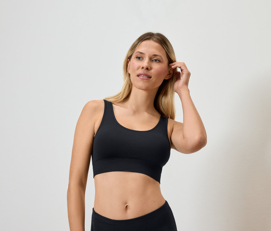 Blonde Frau trägt einen schwarzen Sport-BH und berührt ihr Haar.