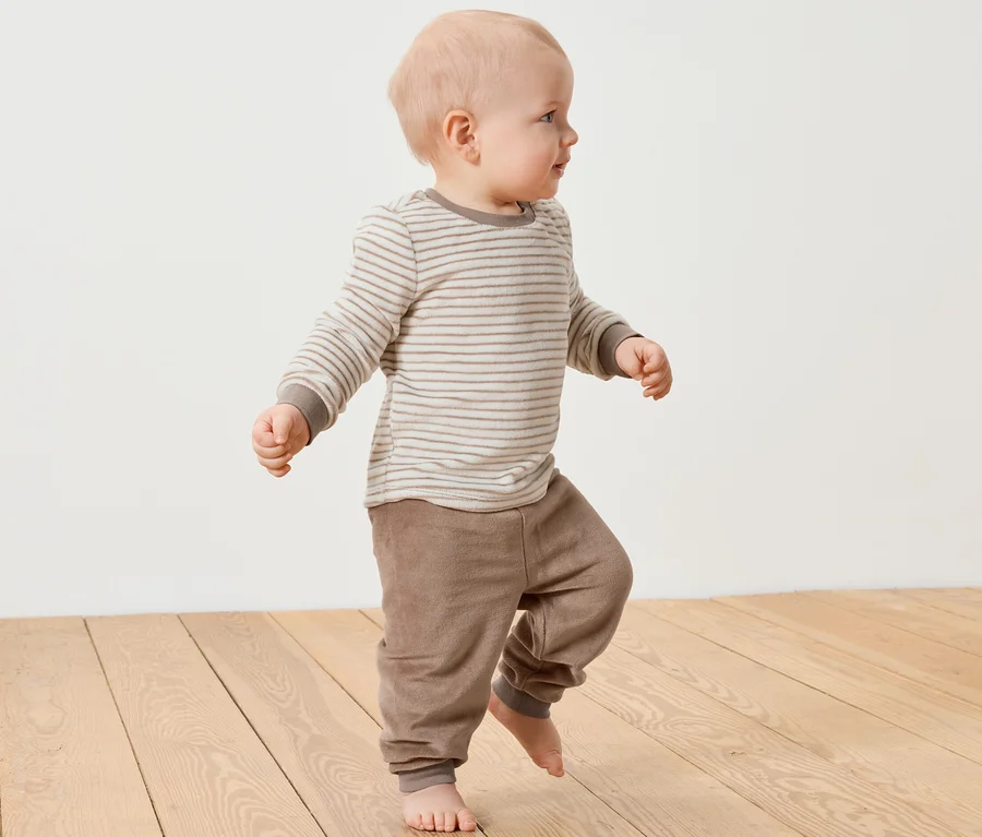 Ein Baby geht auf einem Holzboden und trägt ein Baby-Nicki-Set.