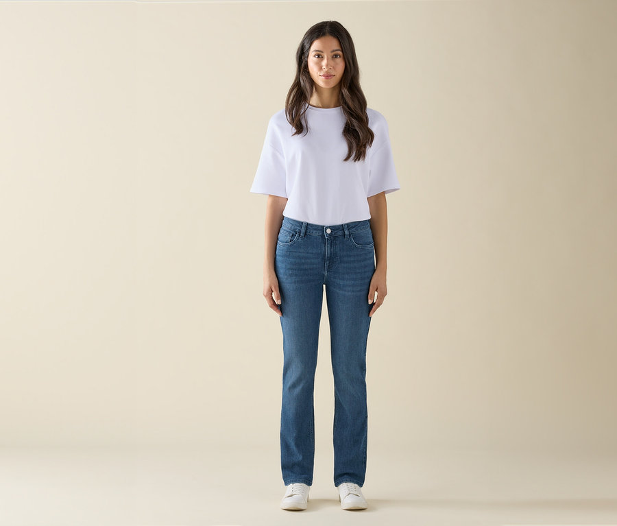 Eine Frau steht und trägt ein weißes T-Shirt, blaue Jeans und weiße Turnschuhe.