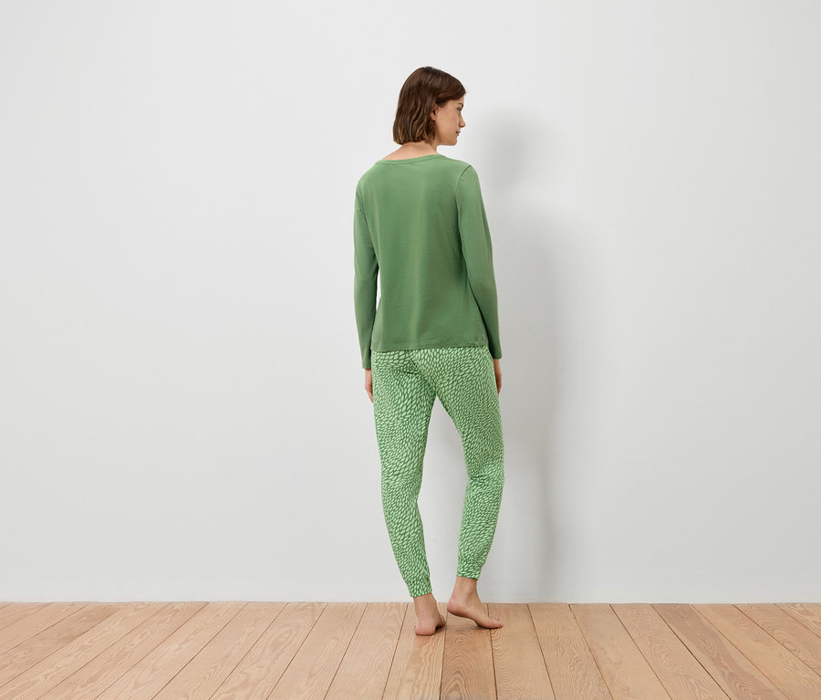 Frau steht mit dem Rücken zur Kamera und trägt einen grünen Pullover und eine grüne Hose.