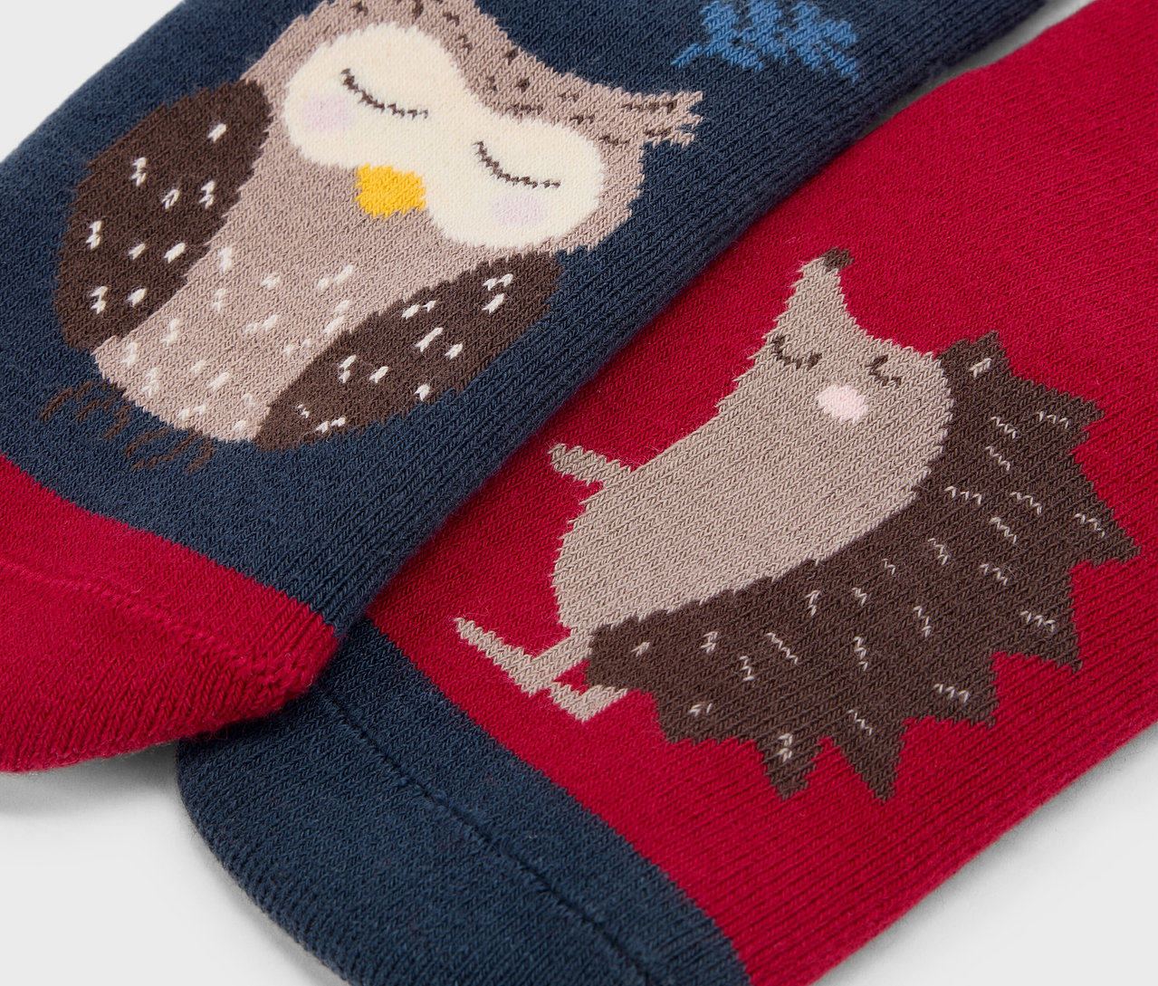 Detailaufnahme von zwei Sockenpaaren. Auf einem ist eine Eule auf blauem Grund, auf dem anderen ein Igel auf rotem Grund.