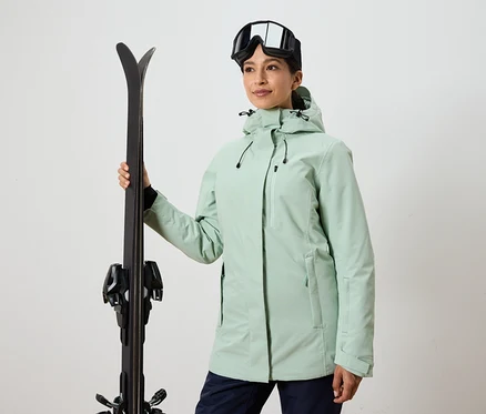 Frau hält Ski und trägt eine Skibrille und eine Jacke.