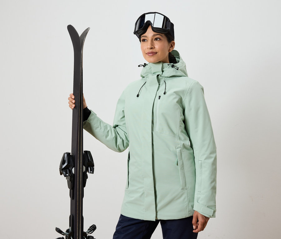 Frau hält Ski und trägt eine Skibrille und eine Jacke.