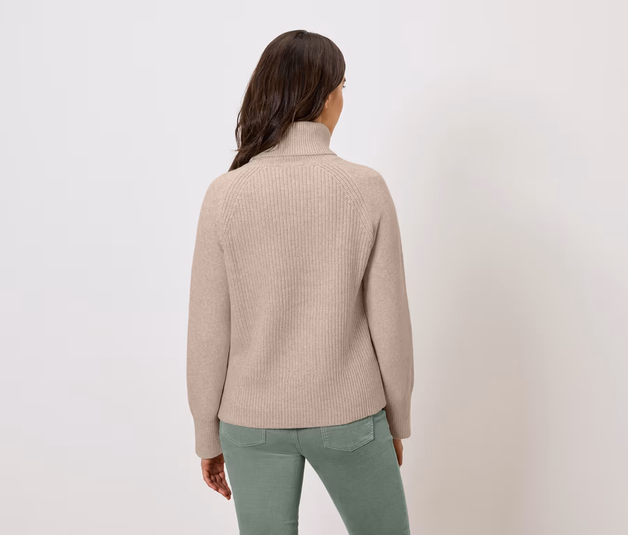 Rückansicht einer Frau mit beigem Rollkragenpullover und grüner Hose.