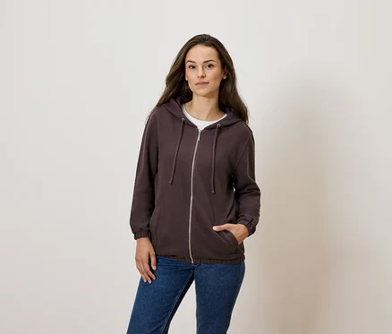 Frau posiert in braunem Reißverschluss-Hoodie und blauen Jeans.