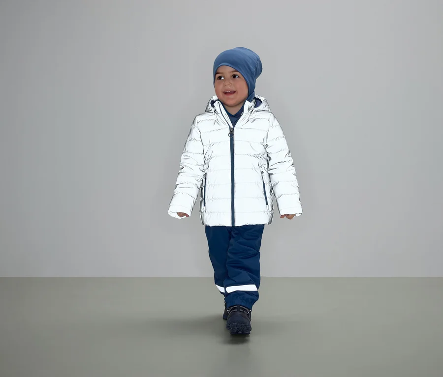 Ein Junge geht in einer weißen Daunenjacke, blauen Hosen und einer Mütze.