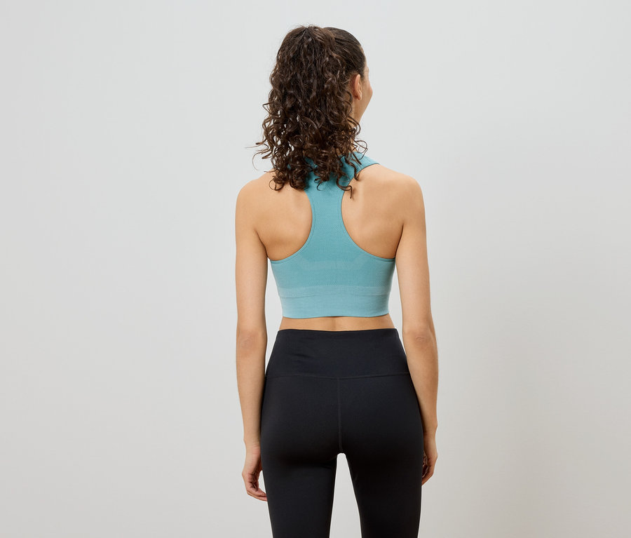 Rückansicht einer Frau mit lockigem Haar, die einen türkisfarbenen Racerback-BH und schwarze Leggings trägt.