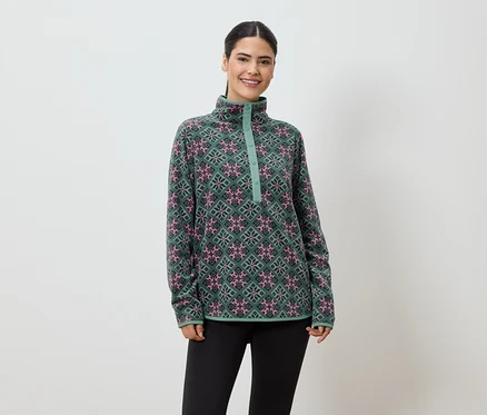 Frau mit Pferdeschwanz trägt einen grünen Fleecepullover mit rosa und schwarzen Mustern und schwarze Leggings vor einem weißen Hintergrund.
