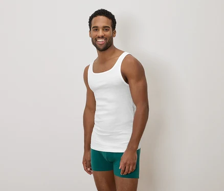 Dunkelhäutiger Mann, der ein weißes Tanktop und grüne Boxershorts trägt und lächelt.