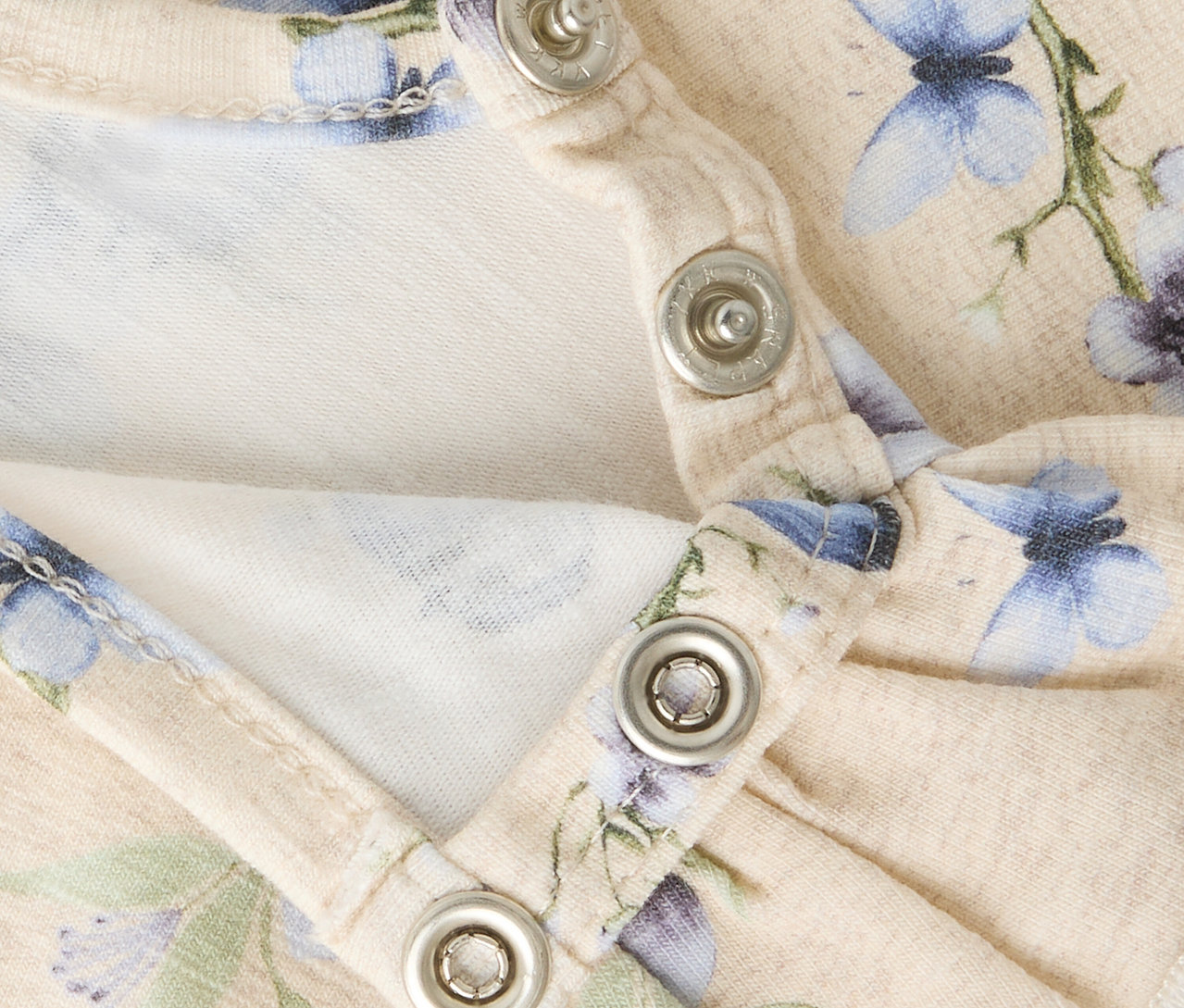 Nahaufnahme von Druckknöpfen am Halsausschnitt eines floralen NAME IT Langarm-Bodys.