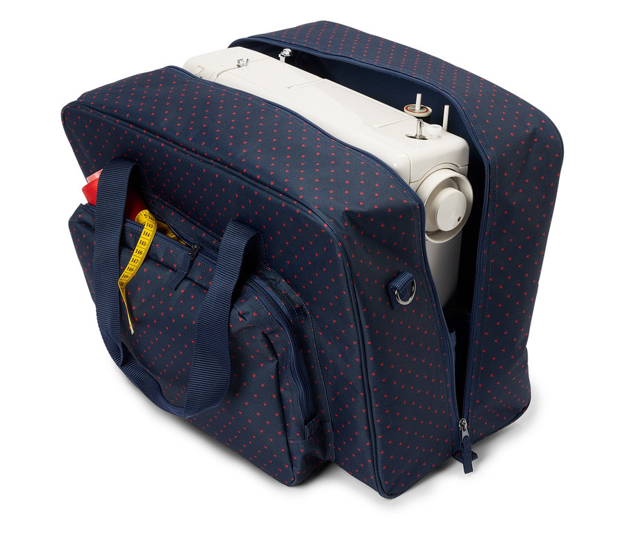Eine weiße Nähmaschine in einer offenen marineblauen Tasche mit roten Herzen. Ein gelbes Maßband ist an der Außentasche befestigt.