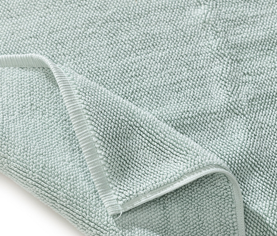 Nahaufnahme einer hellgrünen Badematte mit Textur und umgeschlagener Ecke.