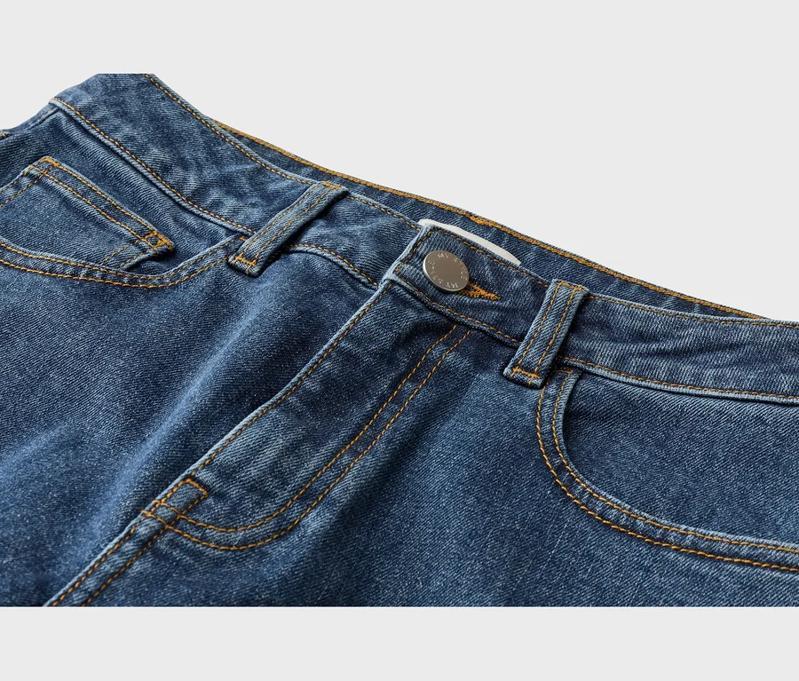 Nahaufnahme des oberen Teils einer blauen Jeans, die Bund, Gürtelschlaufen, Vordertaschen und einen silbernen Knopf mit kontrastierenden orangefarbenen Nähten zeigt.
