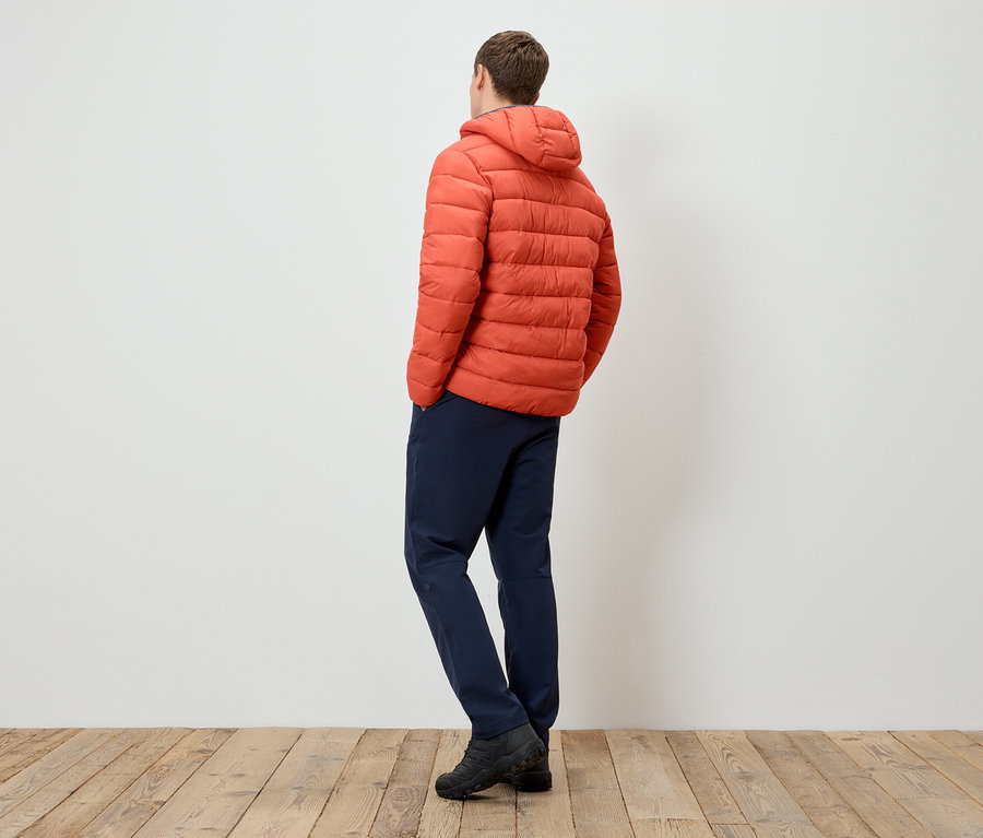 Mann von hinten trägt eine orangefarbene Steppjacke mit Kapuze, marineblaue Hosen und schwarze Stiefel.