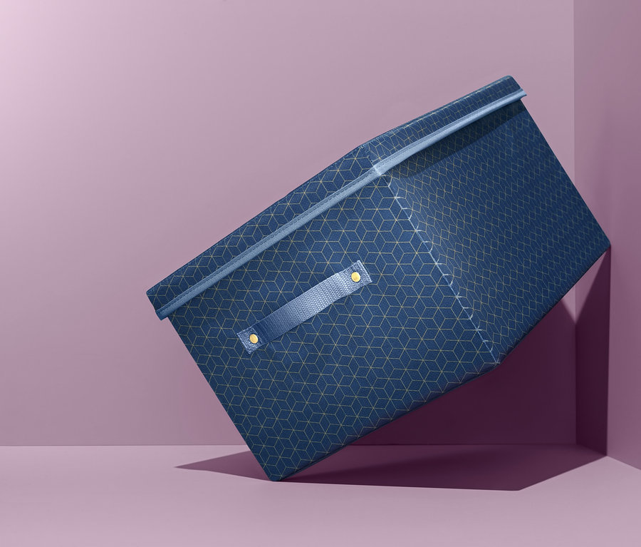 Eine blaue Ordnungsbox mit Deckel liegt schräg in einer Ecke auf violettem Hintergrund.