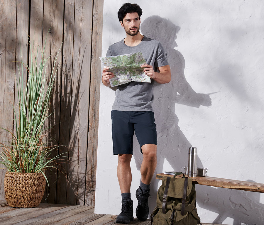 Mann mit grauem T-Shirt und blauen Funktionsshorts studiert eine Karte an einer Holzbank.