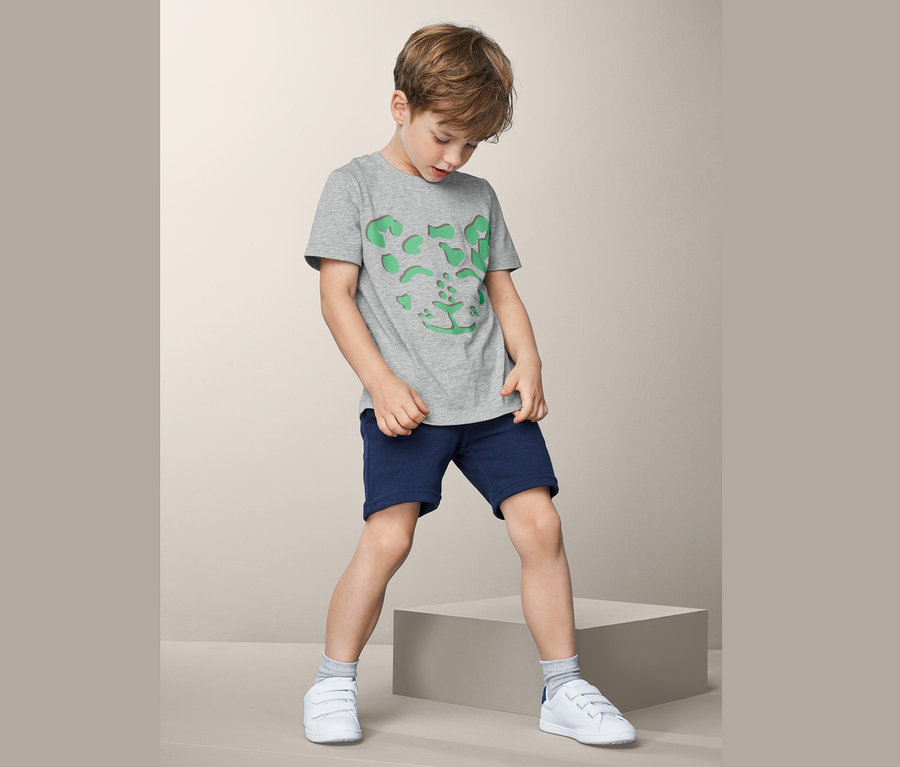Junge mit grauem T-Shirt mit Leopardenmuster und blauen Shorts.