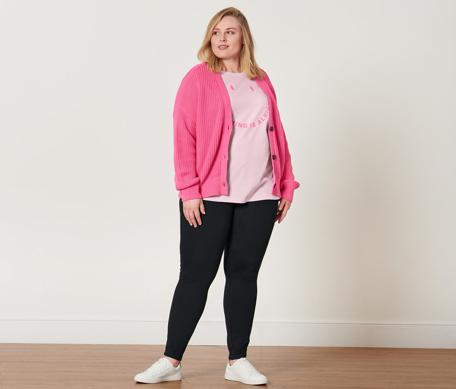Frau posiert in Jeggings, T-Shirt mit Statement-Print, Ledersneaker und Grobstrick-Cardigan.