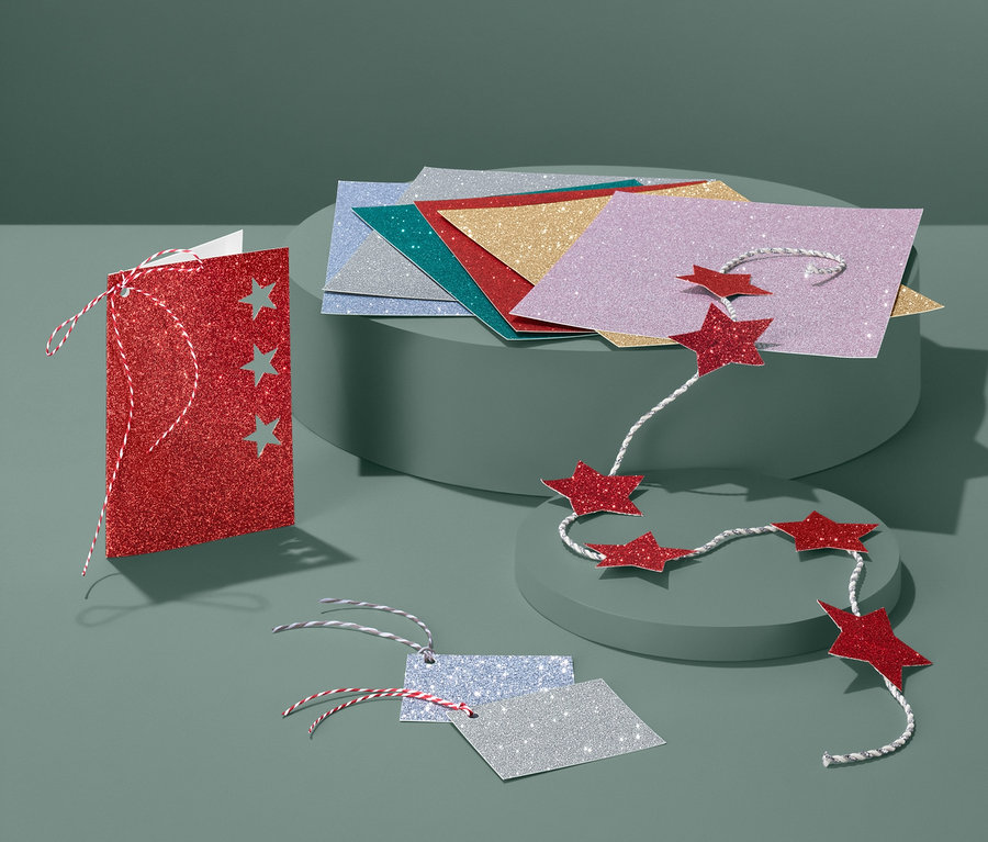 Glitzerpapier-Set auf grünem Hintergrund. Rote Karte mit drei Sternen, ein Satz bunte Papiere und eine Girlande aus roten Sternen.