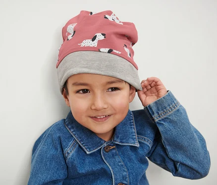 Ein Junge trägt eine rosa-graue Kinder-Wendemütze und eine Jeansjacke.