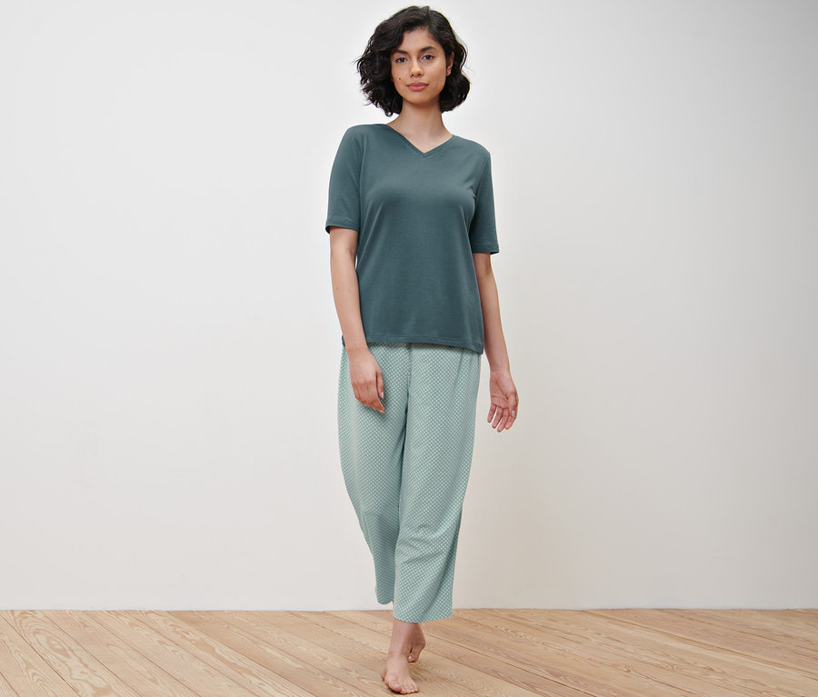 Eine Frau geht und trägt ein grünes T-Shirt und eine Pyjamahose mit Alloverprint.