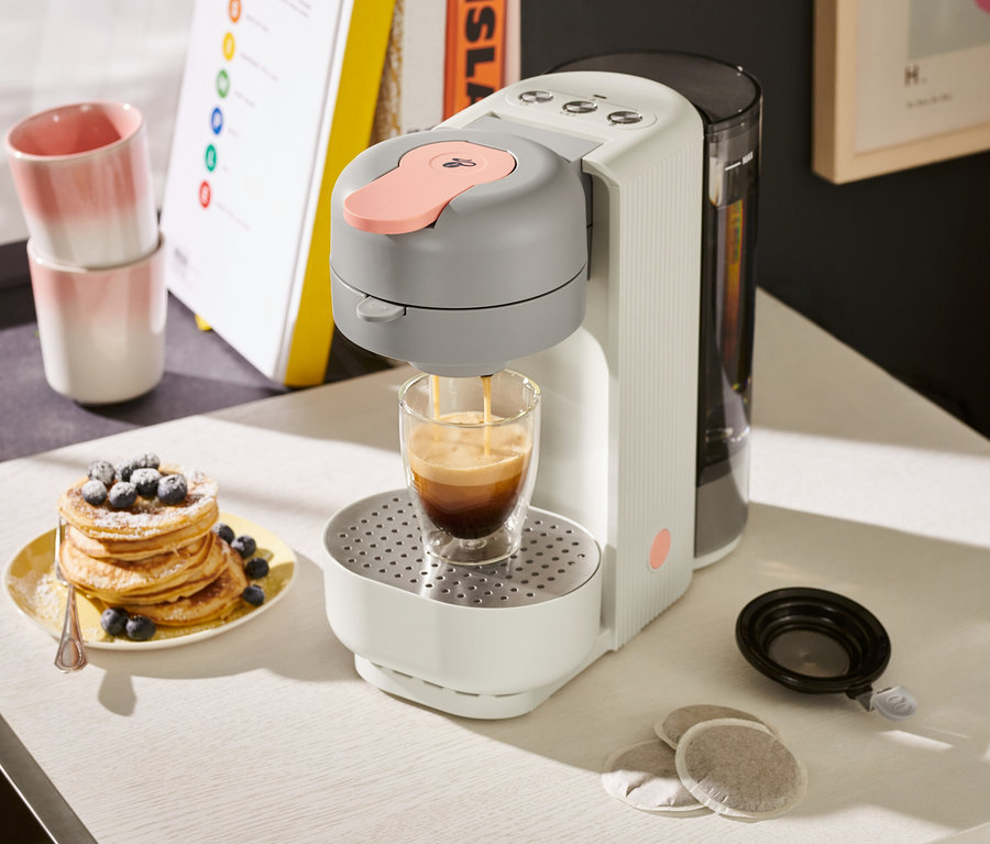 »Call me Pad« Kaffee Padmaschine Soft White bereitet Kaffee in einem Glas neben einem Teller mit Blaubeerpfannkuchen zu.