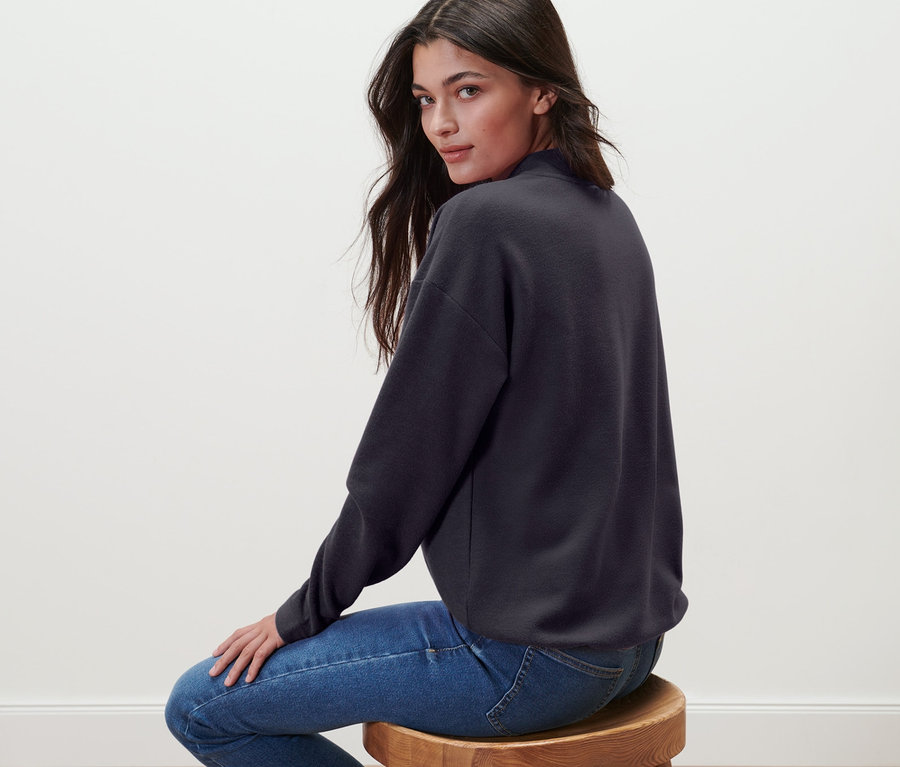 Frau sitzt auf einem Hocker und trägt ein Sweatshirt mit Stehkragen.