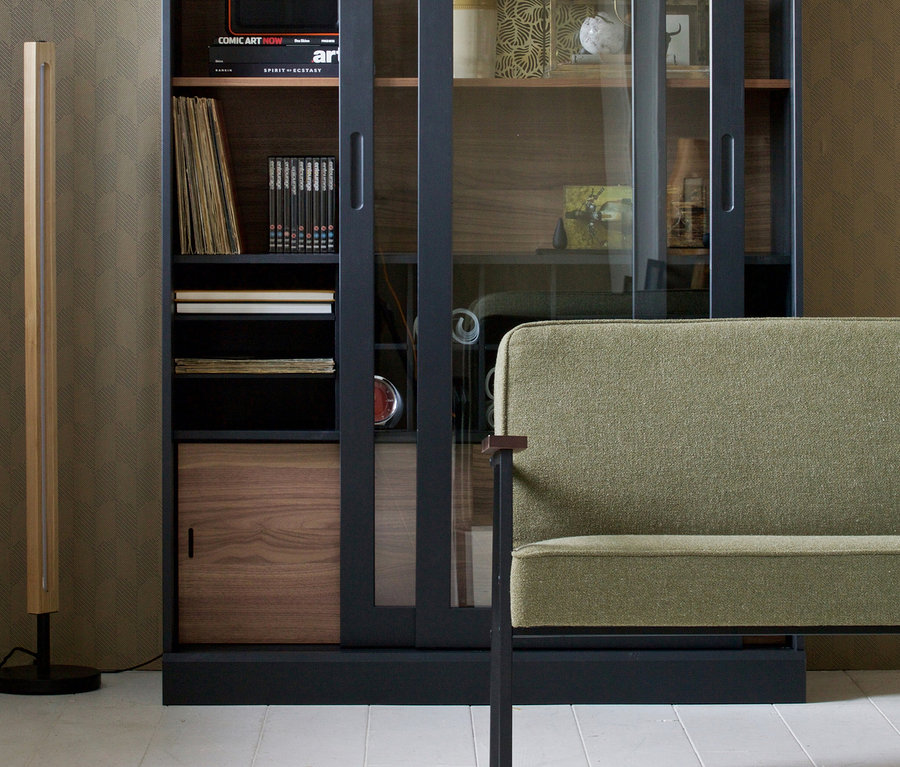 Schwarze Woood Vitrine »James« aus Kiefernholz mit Glasschiebetüren und ein grünes Sofa.