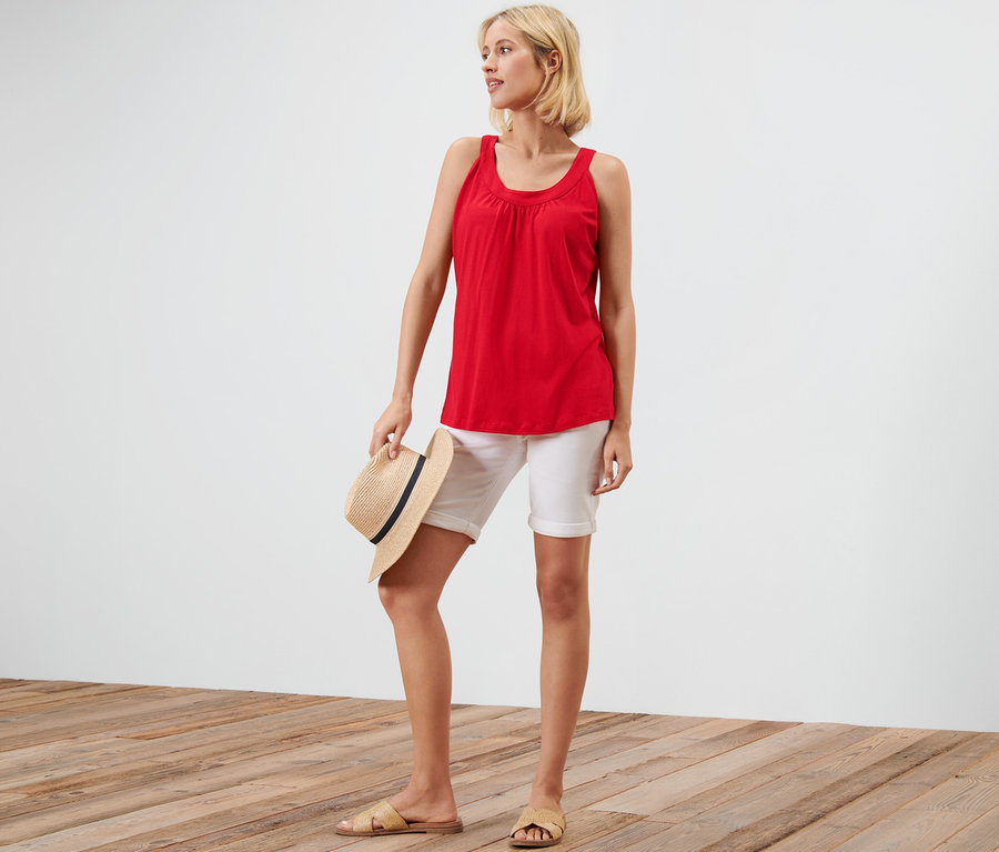 Frau hält einen Hut und trägt ein rotes Top und weiße Shorts.