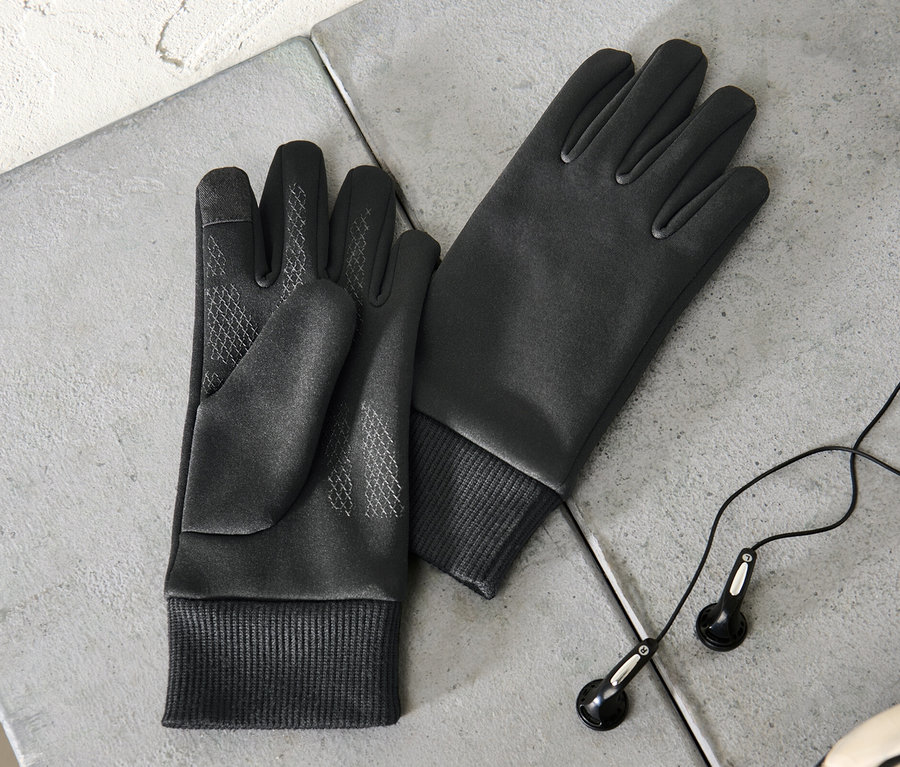 Zwei Kinder-Windprotection-Thermohandschuhe liegen auf einer grauen Oberfläche neben Kopfhörern und einem Teil eines Fußballs.