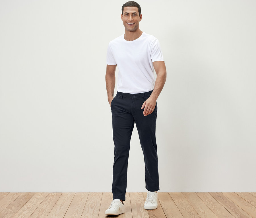 Mann posiert in weißem T-Shirt und dunkelblauer Chino für die Kamera.