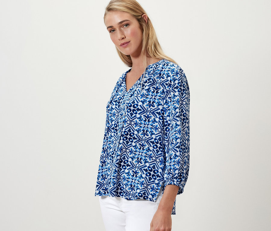 Blonde Frau posiert in blau bedruckter Tunika-Bluse.