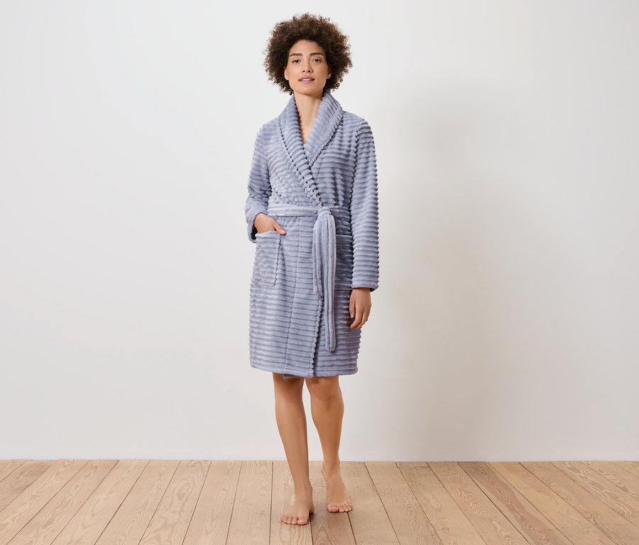 Frau steht auf Holzboden und trägt einen blauen Bademantel.