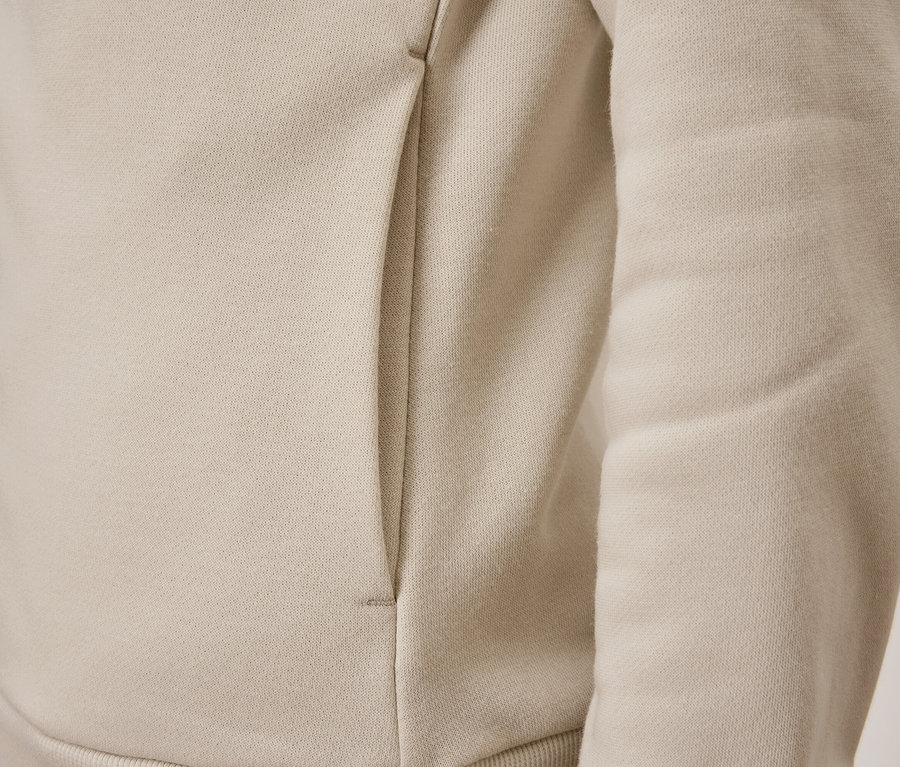 Detailansicht einer beigen Trainingsjacke mit Tasche.