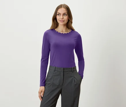 Eine Frau trägt ein violettes Langarmshirt und eine graue Hose.