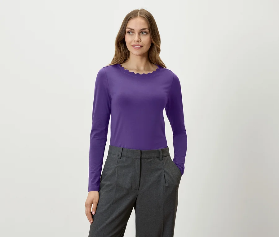 Eine Frau trägt ein violettes Langarmshirt und eine graue Hose.