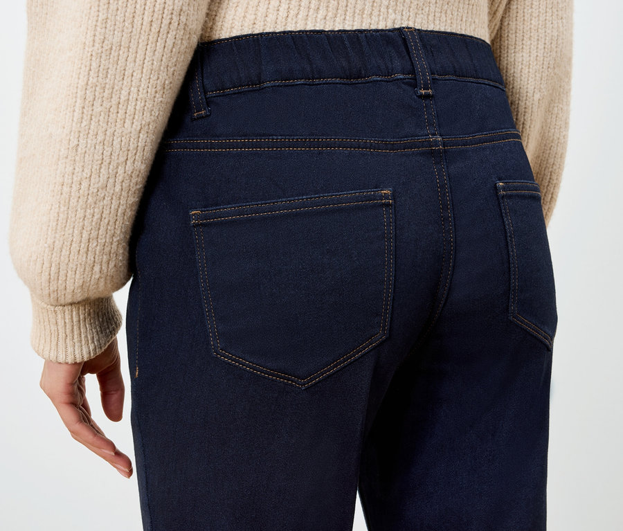 Rückansicht einer Frau in dunkelblauen Jeggings und einem beigen Pullover.