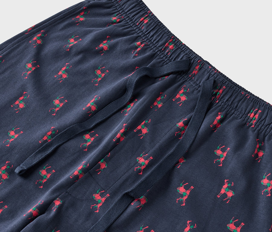 Detail einer blauen Pyjamahose mit roten Rentieren und grünen Sätteln.