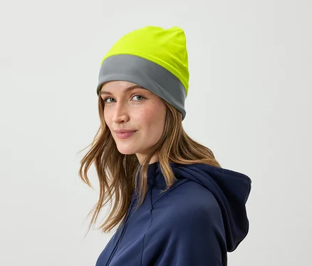 Porträt einer Frau mit braunem Haar und einer grau-gelben Mütze, gekleidet in einem blauen Hoodie.